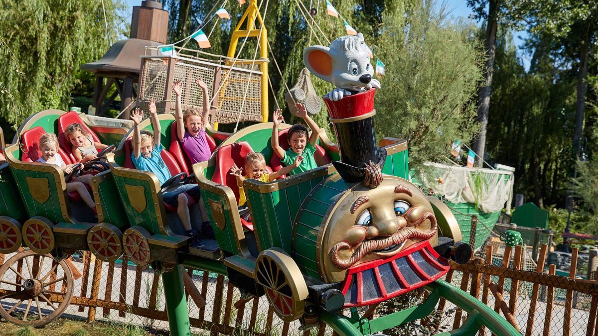Eine Gruppe von Kindern und Erwachsenen fährt in einem bunten Freizeitparkfahrgeschäft mit einem Mauskopf als Fahrer.
